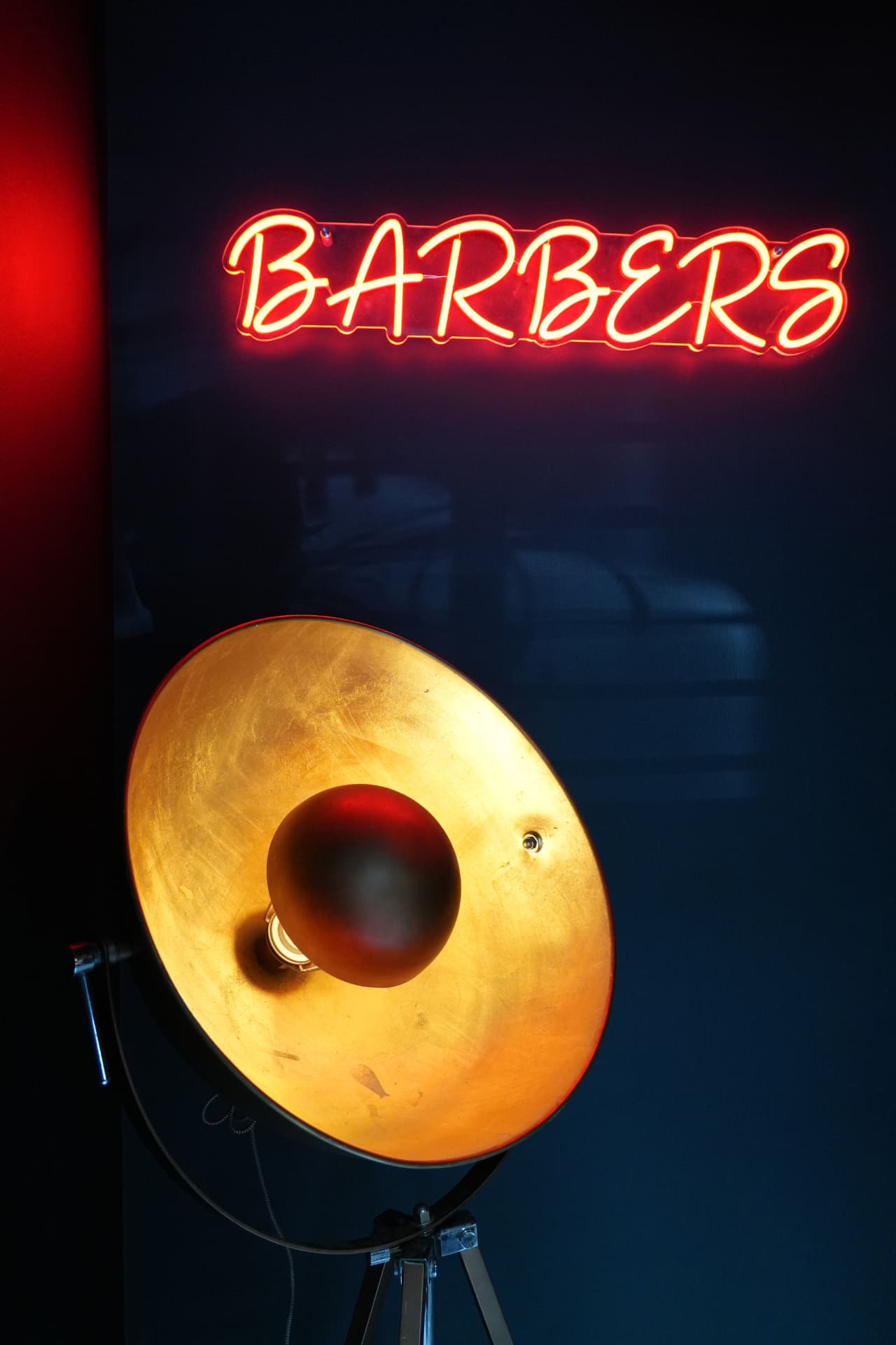 Red neon BARBERS sign above a brass tripod lamp